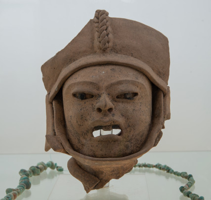 Cabeza escultura hueca de barro con tocado y banda en el maxilar